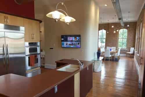 Modern kitchen with stainless steel appliances, a sink, and a living area featuring large windows and stylish furniture.