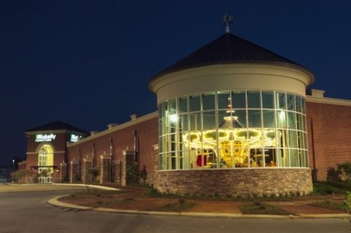 A brightly lit carousel inside a glass structure next to a brick building at night.