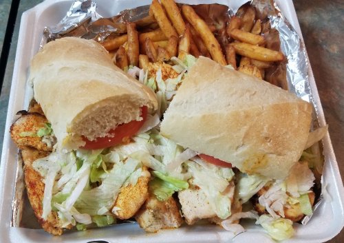A takeout container with two sandwiches filled with chicken, lettuce, and tomato, alongside a serving of fries.