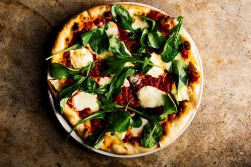 A freshly baked pizza topped with spinach, mozzarella, and tomato sauce on a rustic surface.