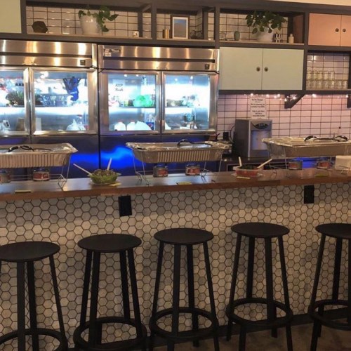 A modern café interior featuring a bar with stools, glass display cases, and a tiled wall.