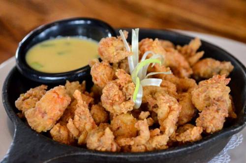 A skillet of crispy fried shrimp garnished with green onions, served with a small bowl of dipping sauce.