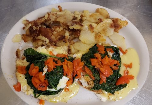 A plate of two poached eggs on spinach with red peppers, served alongside crispy golden-brown hash browns.