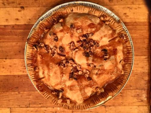 A freshly baked pie with a golden crust, topped with chopped nuts and a glossy glaze, on a wooden surface.