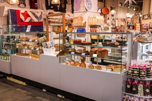 A bakery display with various breads and pastries in a market setting, featuring glass cases and colorful decor.