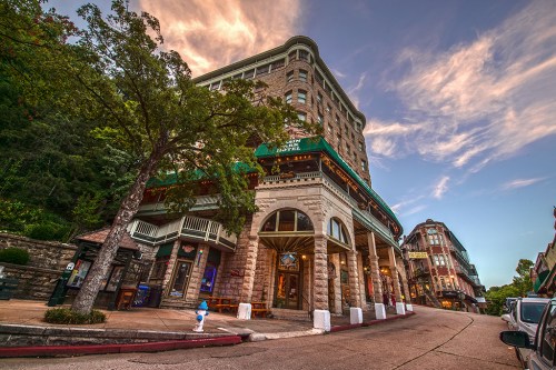 Historic building on a sloped street, surrounded by trees and other architecture, under a colorful sky at sunset.