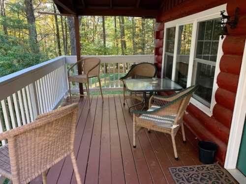 A cozy porch with a glass table and four wicker chairs, surrounded by trees and greenery.