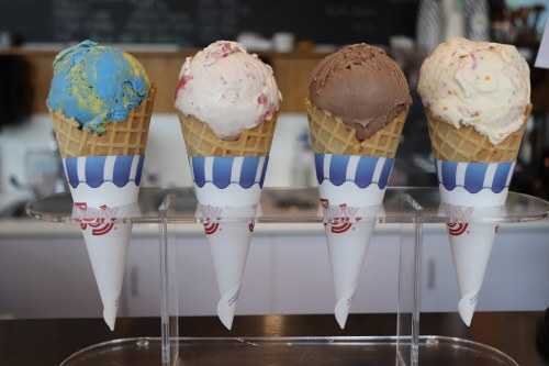 Four ice cream cones in a display, featuring blue, pink, chocolate, and vanilla flavors.