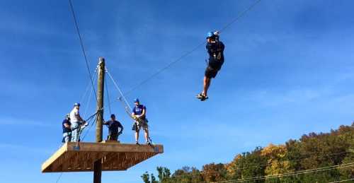 A person zip-lining from a platform while others watch from above on a sunny day.