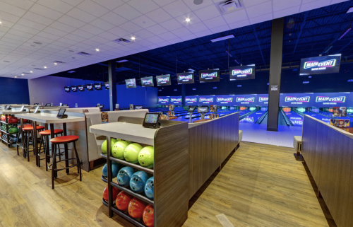 Interior of a bowling alley featuring colorful bowling balls, seating areas, and multiple screens displaying scores.