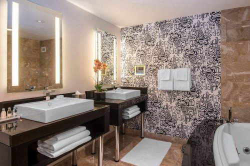 Modern bathroom featuring dual sinks, stylish decor, and a patterned accent wall. Fresh towels and a plant add elegance.