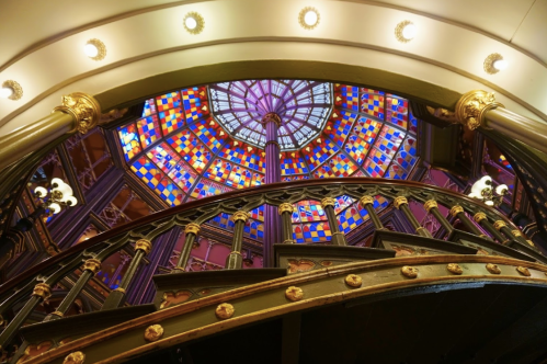 A spiral staircase with ornate railings, leading up to a colorful stained glass dome.