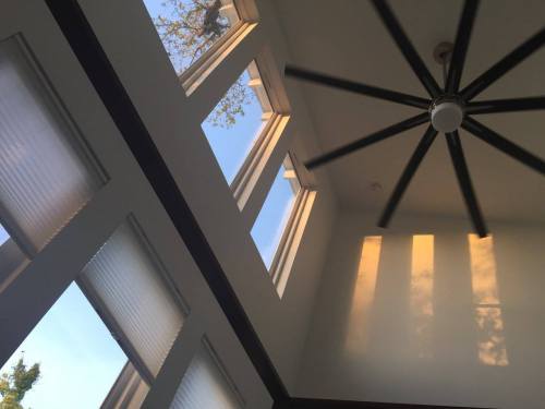 Interior view of a room with large windows, a ceiling fan, and sunlight casting shadows on the walls.