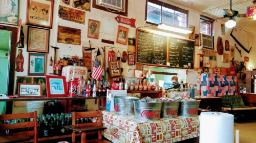 A vintage diner interior with memorabilia on the walls, a menu board, and a table covered in Coca-Cola items.
