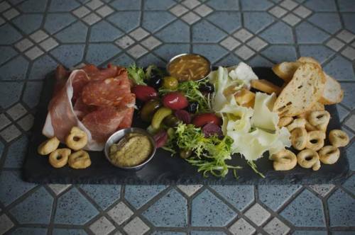 A charcuterie board featuring meats, cheeses, olives, bread, and dips on a textured surface.