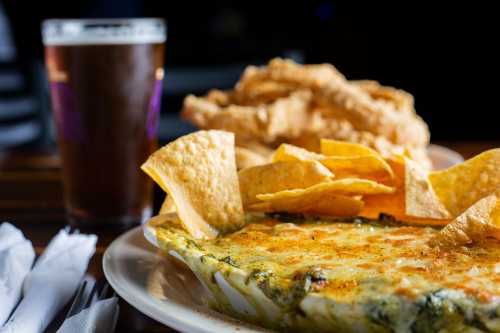 A plate of cheesy spinach dip with tortilla chips, accompanied by fried chicken and a glass of beer.