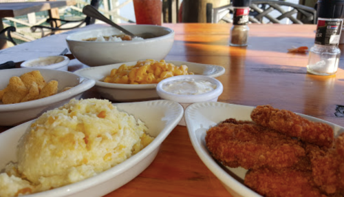 A table set with bowls of mashed potatoes, macaroni and cheese, fried chicken, and snacks, with condiments nearby.