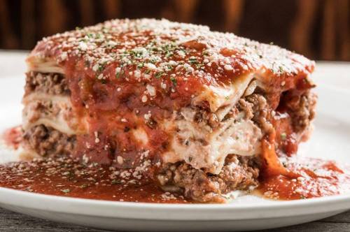 A hearty slice of lasagna layered with meat, cheese, and marinara sauce, garnished with herbs and grated cheese.