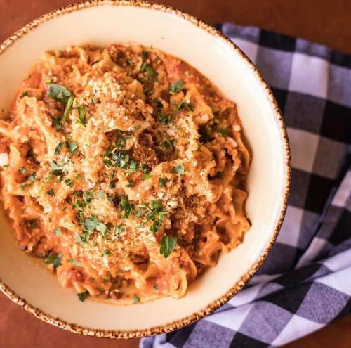 Creamy pasta dish topped with herbs and breadcrumbs, served in a bowl next to a checkered napkin.