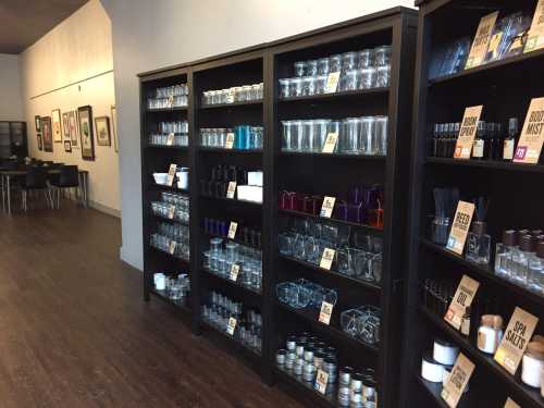 Shelves filled with various glassware and bottles, labeled with signs, in a well-lit store interior.