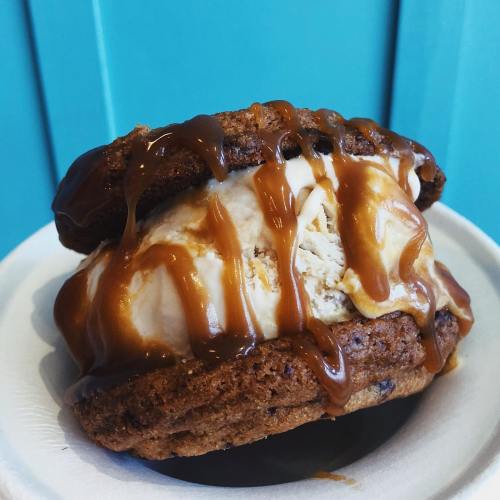 A delicious ice cream sandwich made with chocolate chip cookies and drizzled with caramel sauce on a paper plate.