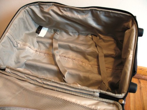 An empty suitcase with a beige interior and straps, resting on a wooden surface.