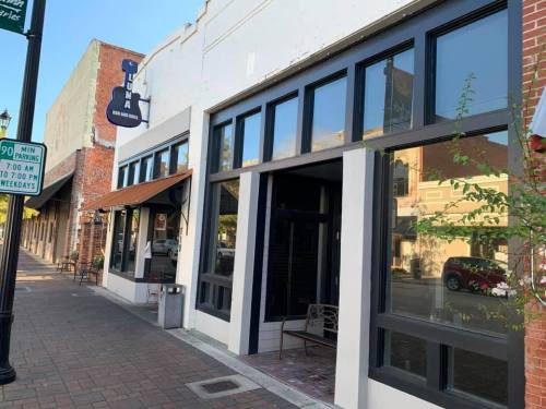 Exterior of a building with large windows and a sign, featuring a sidewalk and street view in a quaint town setting.