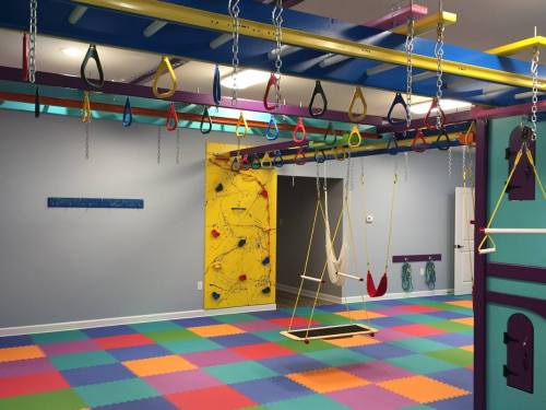 Colorful indoor playroom with climbing equipment, swings, and a padded floor, designed for children's activities.