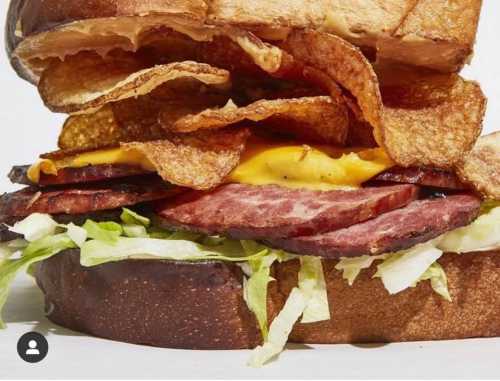 A close-up of a sandwich with layers of meat, cheese, lettuce, and potato chips on toasted bread.