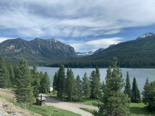Scenic view of a lake surrounded by mountains and dense pine trees under a partly cloudy sky.
