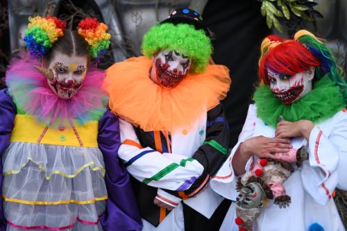 Three clowns with colorful wigs and elaborate makeup, wearing vibrant costumes and eerie expressions.