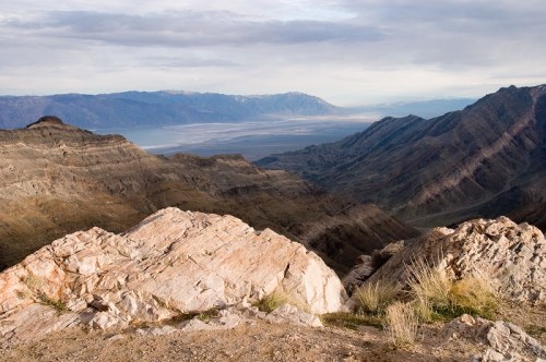 A panoramic view of rugged mountains and valleys under a cloudy sky, showcasing natural rock formations and distant peaks.