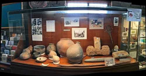 Display case featuring various ancient pottery, tools, and artifacts in a museum setting.