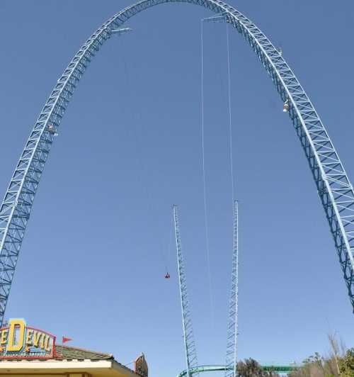 A tall blue amusement park ride against a clear sky, with a small cart suspended from the top.