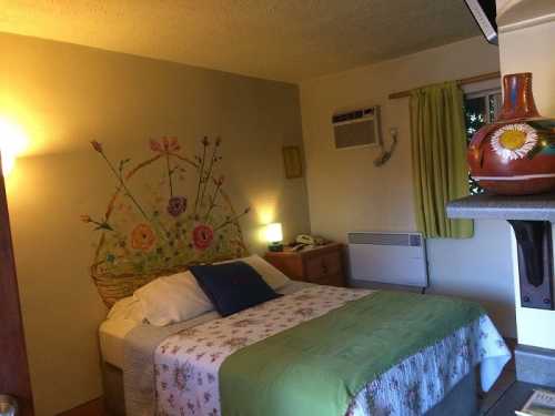 Cozy bedroom with a floral mural, a double bed, and warm lighting, featuring green curtains and a decorative vase.