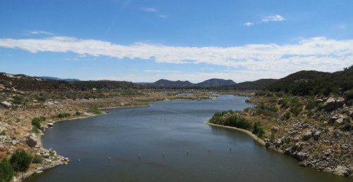 A serene landscape featuring a winding river surrounded by hills and blue skies with scattered clouds.
