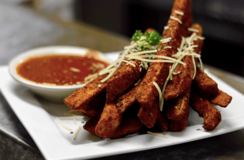 A plate of crispy, spiced fries topped with grated cheese, served with a side of dipping sauce.