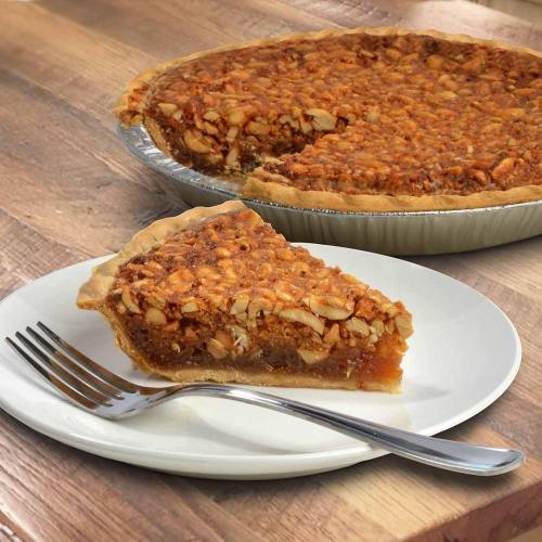 A slice of pecan pie on a white plate with a fork, next to a whole pie on a wooden table.