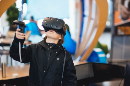 A child wearing a VR headset, holding controllers, immersed in a virtual reality experience indoors.