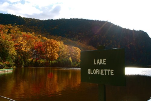 A serene lake surrounded by autumn foliage, with a sign reading "Lake Gloriette" in the foreground.