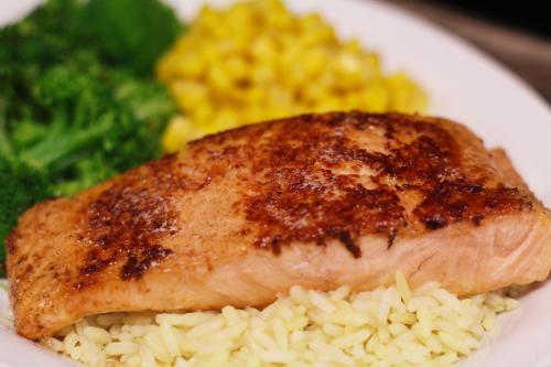 A plate featuring a piece of grilled salmon on a bed of rice, accompanied by broccoli and yellow corn.