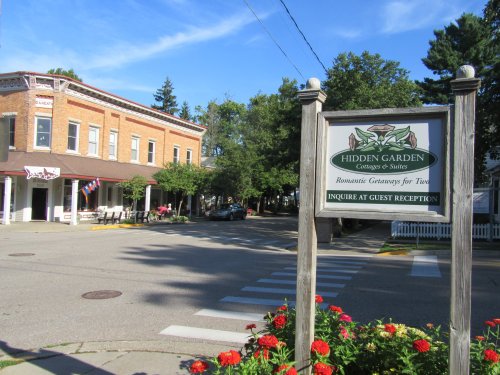 A street view featuring a sign for Hidden Garden Cottages & Suites, with a brick building and flowers in the foreground.