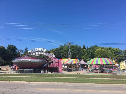 Colorful carnival rides and attractions under a clear blue sky, with trees in the background.