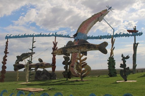Colorful wooden fish sculptures on a grassy field, with a blue sky and clouds in the background.