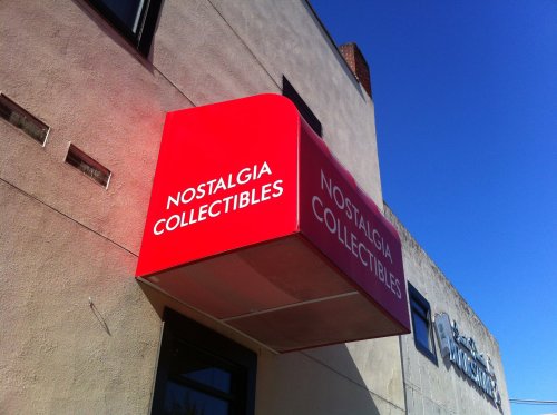 Red awning with the text "NOSTALGIA COLLECTIBLES" on a building exterior against a clear blue sky.