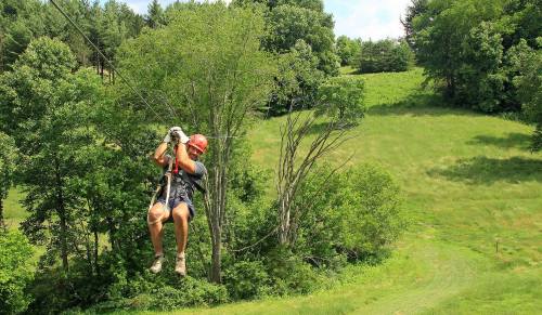 A person in a helmet zip-lining through a lush green landscape with trees and hills in the background.
