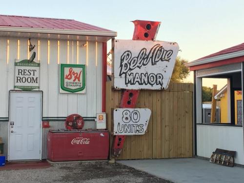 Sign for Bel Vue Manor with "80 Units" next to a building featuring a Coca-Cola cooler and a rest room entrance.