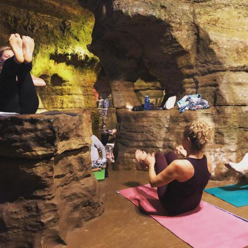 A yoga class takes place in a cave, with participants practicing poses on mats surrounded by rock formations.