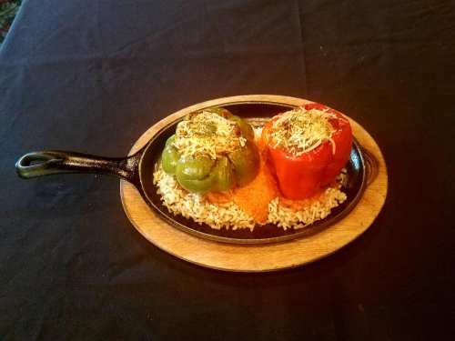 A cast iron skillet with stuffed green and red bell peppers on a bed of rice, garnished with herbs.