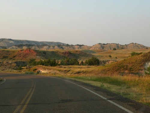 A winding road leads through grassy hills and colorful rock formations under a clear sky.